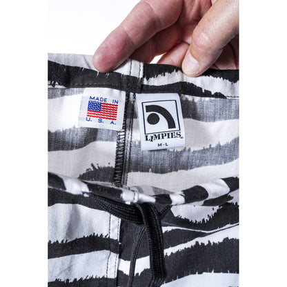 Close-up of a person's hand holding the waistband of patterned baggy skate pants, showing the interior labels including a 'Made in U.S.