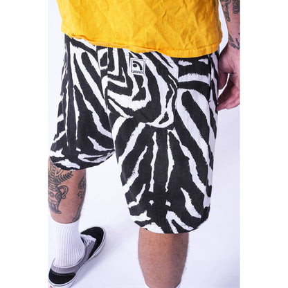 A person wearing black and white zebra-print baggy skate shorts, a yellow shirt, white socks, and black sneakers, photographed against a plain white studio background.