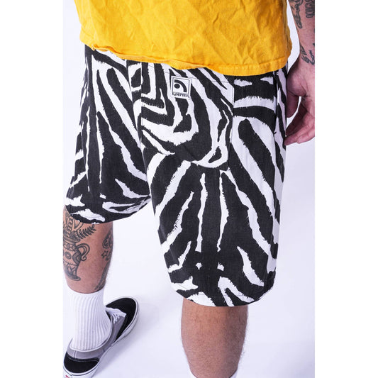 A person wearing black and white zebra-print baggy skate shorts, a yellow shirt, white socks, and black sneakers, photographed against a plain white studio background.