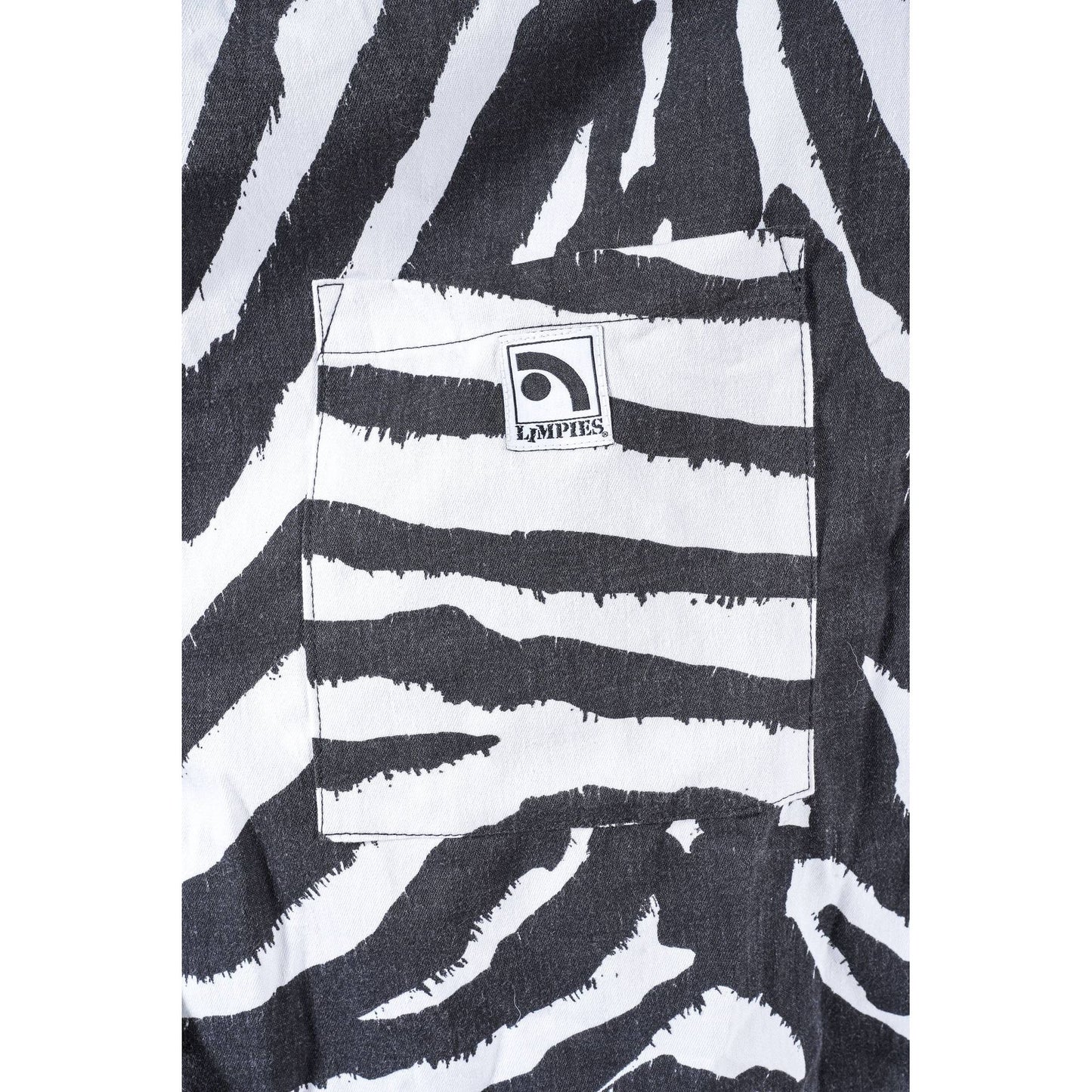 Close-up of black and white zebra-print baggy skate shorts featuring a front pocket with a visible square patch logo that reads 'Limpies'.