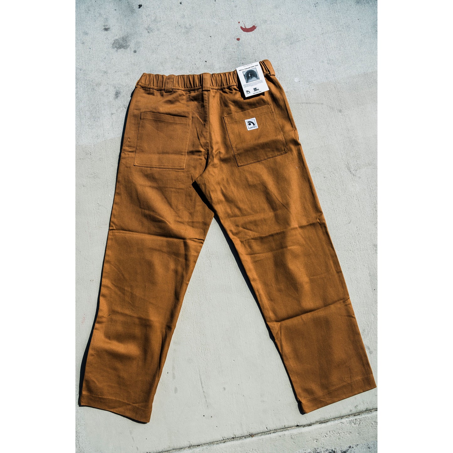 Brown baggy skate pants with a brand tag on a concrete surface