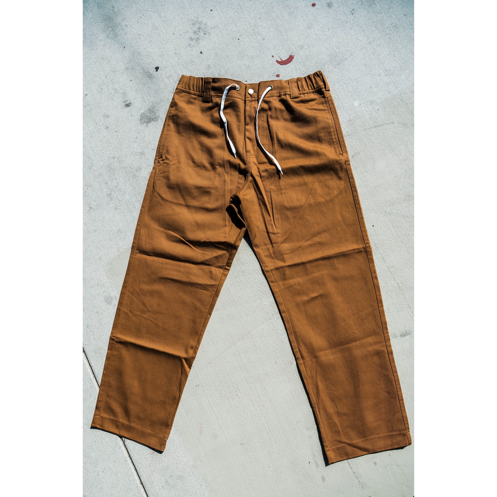 Brown baggy skate pants with white drawstrings on a gray concrete floor