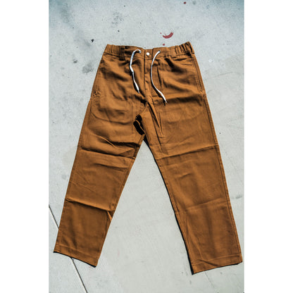 Brown baggy skate pants with white drawstrings on a gray concrete floor