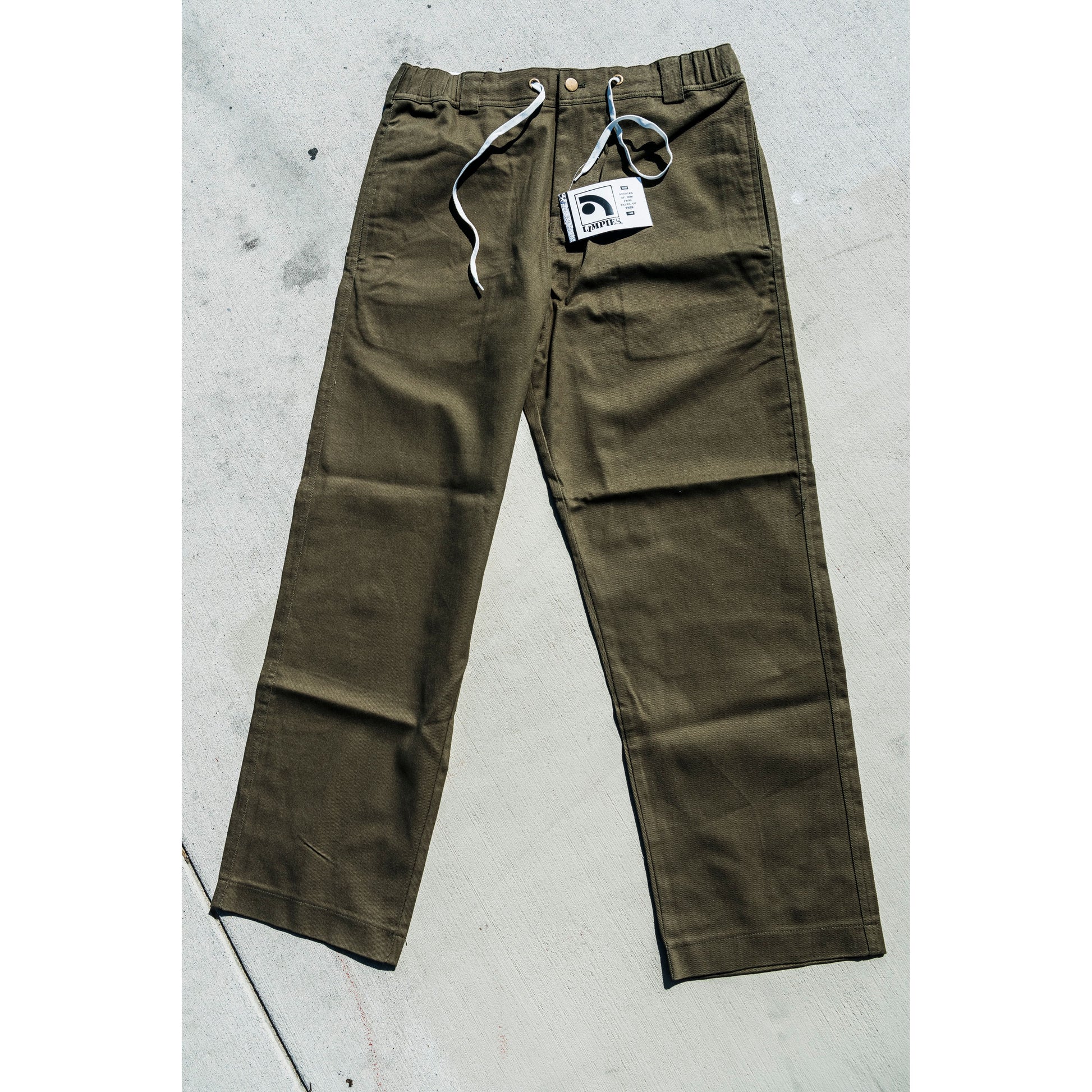 olive Green baggy skate pants with a tag on a gray concrete surface