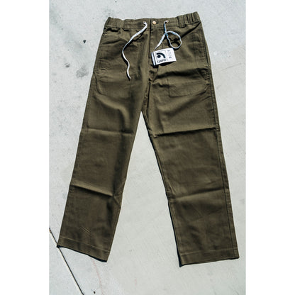 olive Green baggy skate pants with a tag on a gray concrete surface