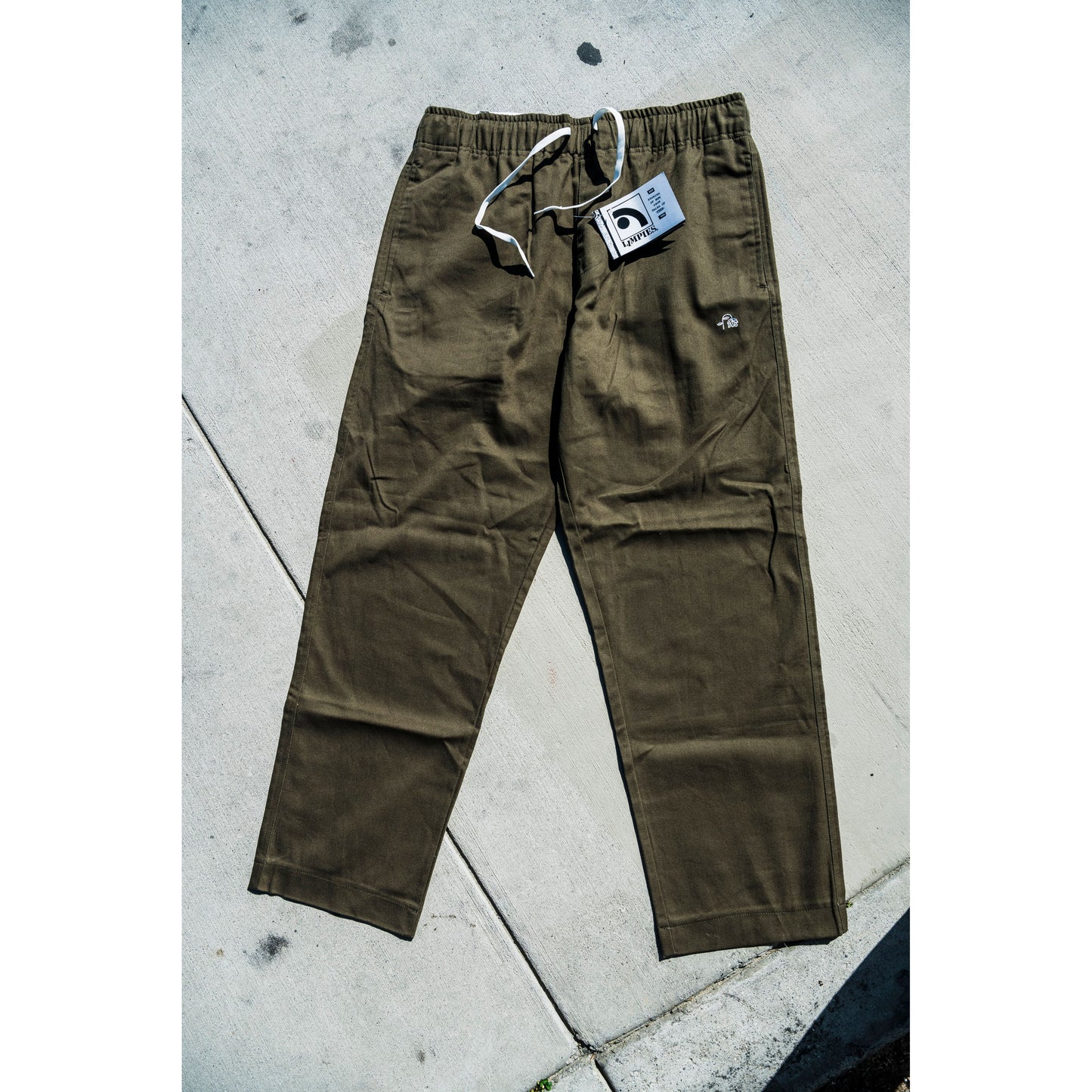 olive green baggy skate pants with a tag on a concrete surface