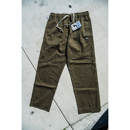 olive green baggy skate pants with a tag on a concrete surface